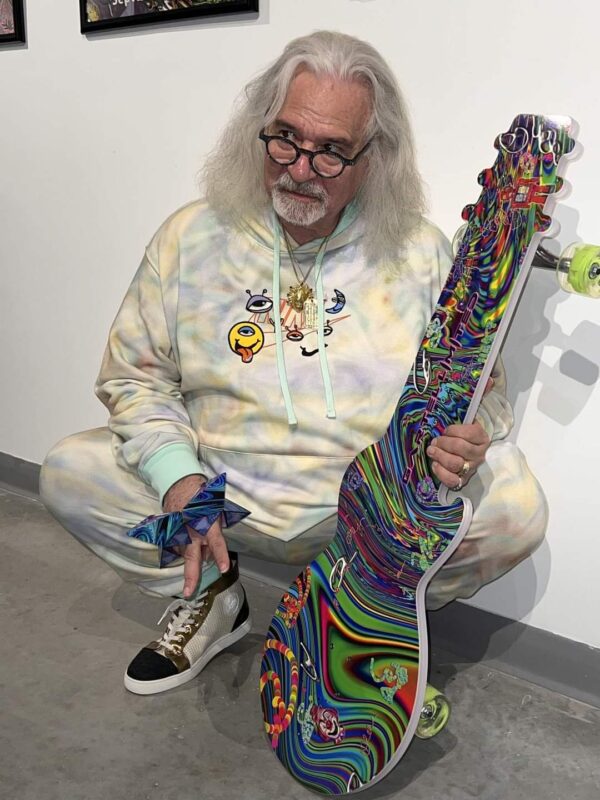 Laurence Gartel holding a Ghost Board Guitar board with his limited edition art on the longboard.